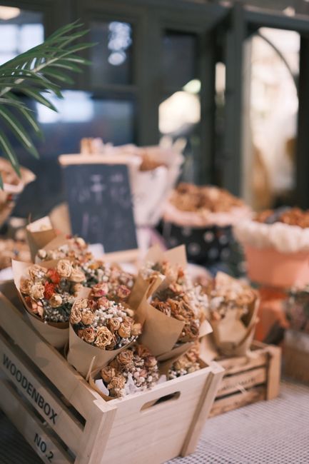 A display of dried flower bouquets arranged in light-colored paper wrappers inside a wooden crate labeled 'WOODENBOX NO.2'. The bouquets feature a mix of beige, brown, and muted pink tones, with textu