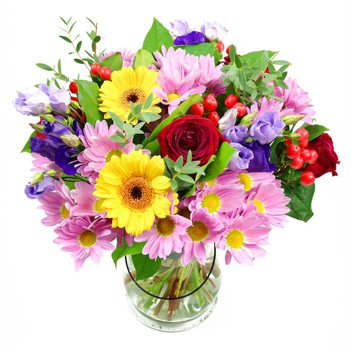 A tall, rounded bouquet of mixed garden blooms rises from a clear glass vase, its colours glowing all the more intensely against a crisp white background, as if it has just been placed on a bright windowsill in Bromley Common. Dominating the centre are rich, deep red roses, their layered, velvety petals conveying warmth and affection. They are flanked by two golden yellow gerbera daisies with distinct dark brown-orange centres, their broad, flat faces turned outward like happy little sunbursts. Around this central cluster, soft pink daisies and chrysanthemums spread in feathery profusion, each flower with many fine petals radiating from a small yellow heart, adding a gentle, almost cloud-like texture to the design. Woven through these pastel tones are slender stems of purple and lavender lisianthus, their bell-shaped blooms curling delicately at the edges, introducing cooler notes that balance the composition the way evening shade balances sun in nearby Queensmead Recreation Ground. Small tufts of bright red hypericum berries peek out from between leaves and petals, their smooth, rounded forms bringing a playful, contemporary touch. The foliage, in varied greens from deep emerald to fresh lime, fills and frames the bouquet, with broad leaves giving structure and lighter sprigs adding movement and airiness. The transparent vase shows the cleanly trimmed stems gathered neatly in clear water, emphasising the bouquet's hand-crafted nature and the florist's attention to every detail. Evoking joy, gratitude, and celebration, this mixed arrangement feels perfect for birthdays, get-well wishes, or a surprise delivery to a Bromley Common doorstep, infusing living rooms and kitchens with colour, life, and a sense of thoughtful care.